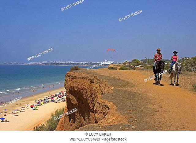 Algarve  Praia de Falesia Couple riding along cliffs with beach below and paraglider flying iin distance behind