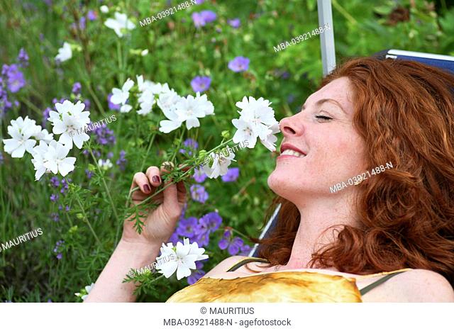 Young woman on sun bed, smelling at flower
