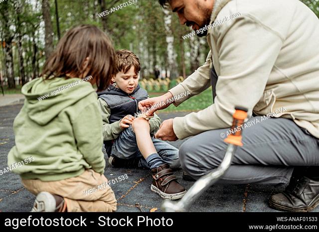 Father putting band aid on son's wound at park