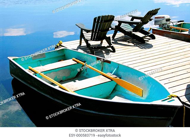 Paddle boat and two adirondack wooden chairs on dock facing a blue lake