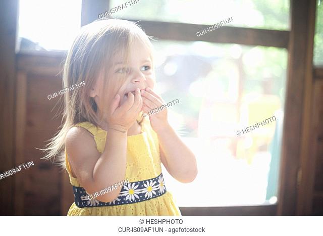 Close up of female toddler with hands over mouth
