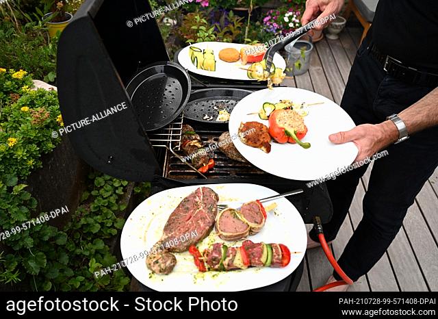 24 July 2021, Baden-Wuerttemberg, Stuttgart: A man lies with a pair of tongs grilled food on a plate. Photo: Bernd Weißbrod/dpa