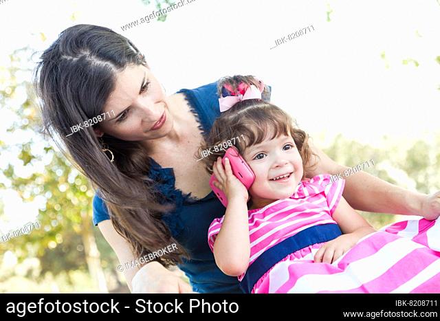 mixed-race mother and cute baby daughter playing with cell phone in park