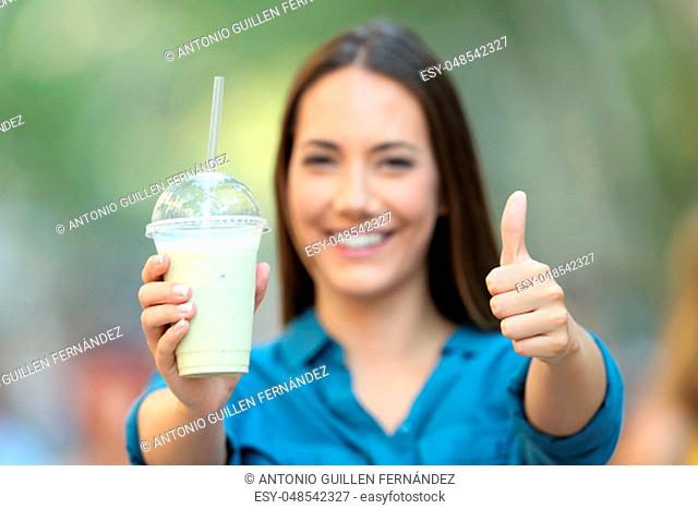 Front view portrait of a satisfied woman holding a smoothie with thumbs up