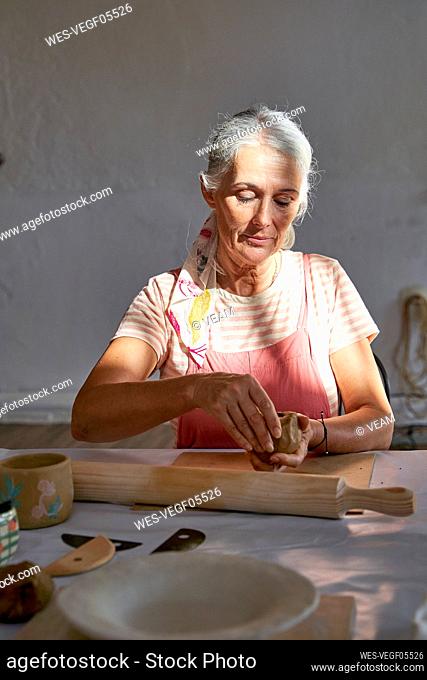 Woman with gray hair making clay mug at home