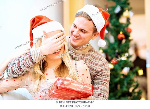 Young man covering girlfriends eyes whilst handing christmas present