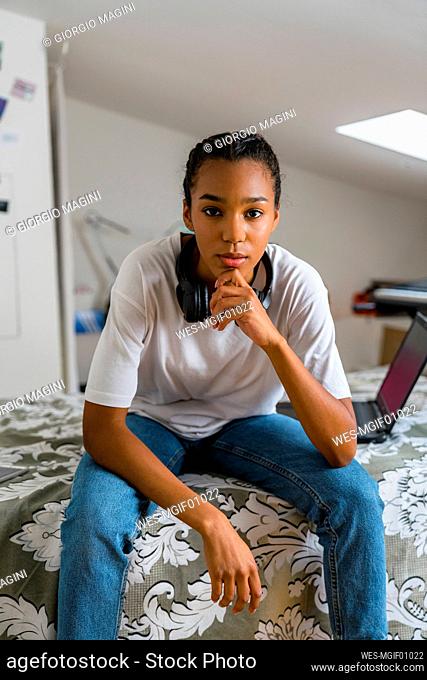 Teenage girl with hand on chin sitting in bedroom at home