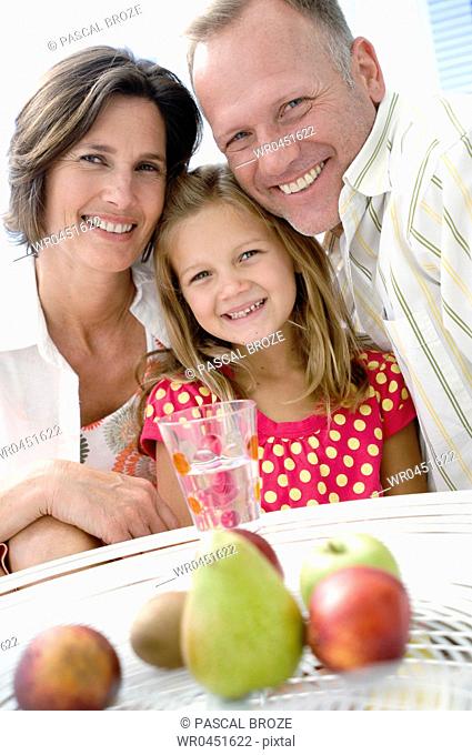 Portrait of a mid adult couple and their daughter smiling with fruits before them