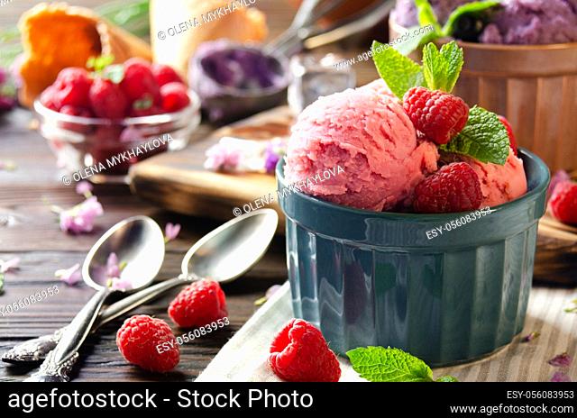 Pink Raspberry icecream balls in clay bowls on wooden kitchen table with berries and spoons aside
