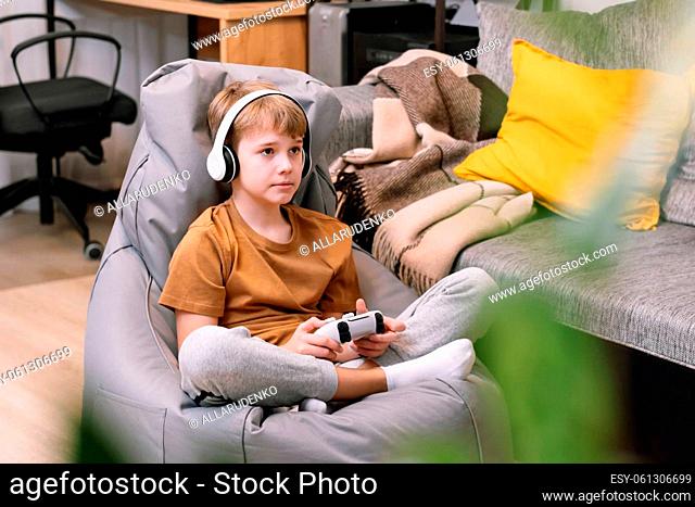 Portrait of teen boy actively and recklessly playing video game with joystick sitting on frameless beanbag chair at home