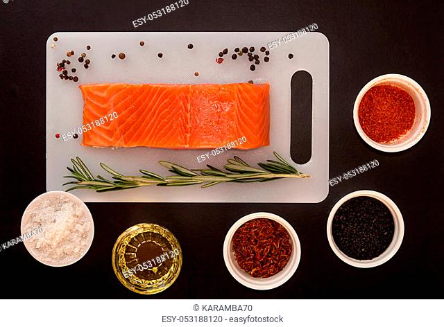 Salmon fillet on white chopping board and seasoning in bowl over on black background. Healthy food concept. Top view