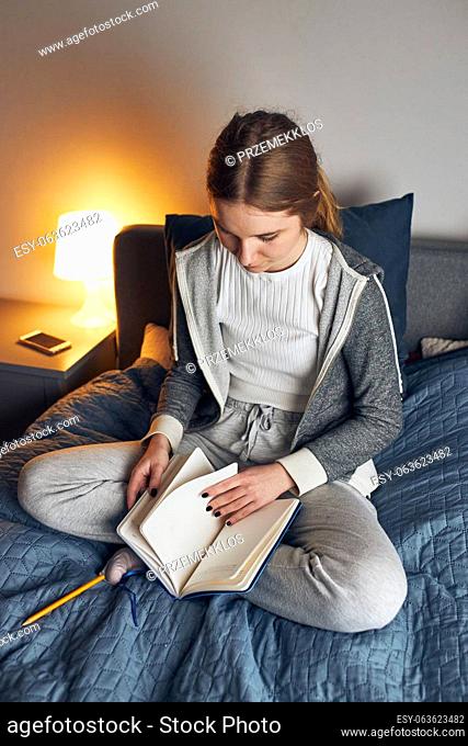 Student learning at home. Young woman making notes, reading and learning from notepad sitting in bed at home during quarantine