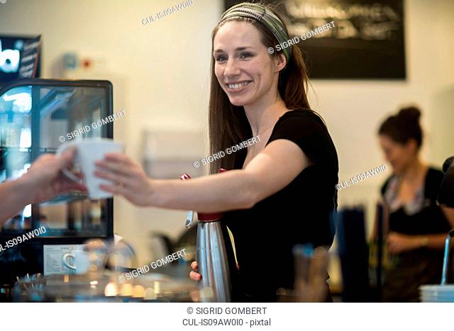 Young female waitress handing cup of coffee to cafe customer