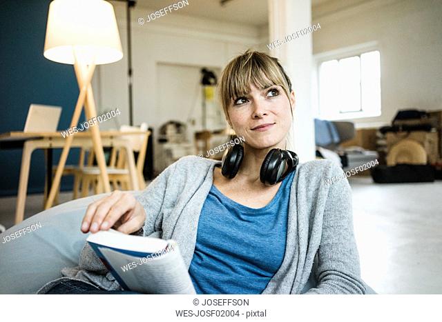 Smiling woman sitting in beanbag with book and headphones