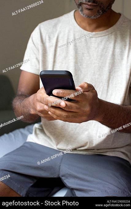 Man using smart phone while sitting in bedroom