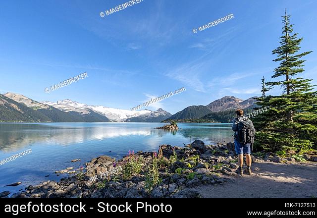 Hikers on the shore of Garibaldi Lake, mountains reflected in the turquoise glacial lake, Guard Mountain and Deception Peak, glacier in the back