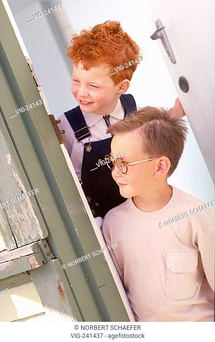 portrait, half-figure, funny redheaded boy with freckles, wearing white shirt and blue trousers with flap and blond boy with spectacles looking interested from...
