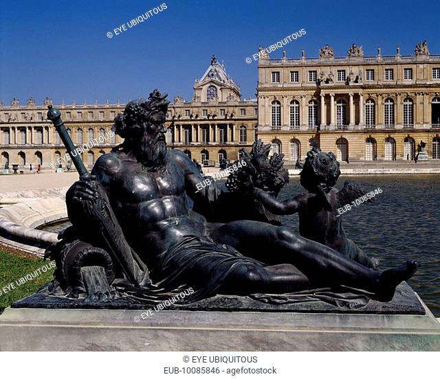 Versailles . Part view of palace behind bronze reclined statue of man with child next to pond