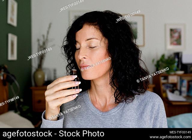 Woman smelling essential oil from bottle at home