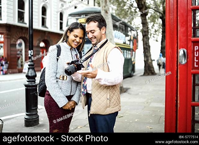 Happy traveling couple looking at photos on their camera, London, Great Britain