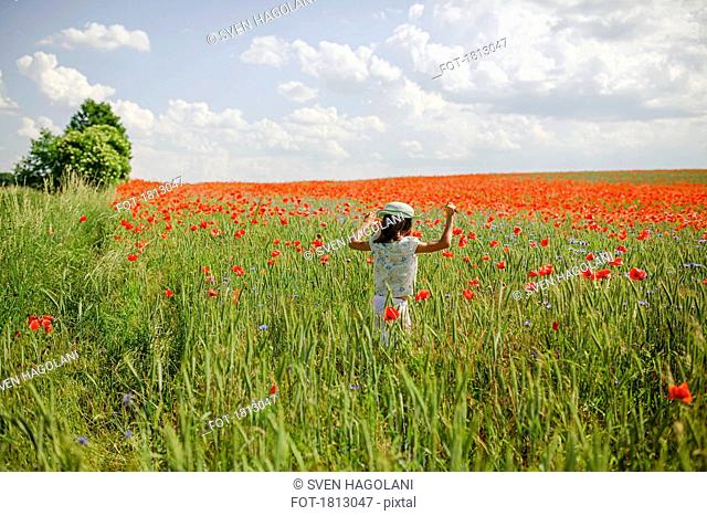 Girl running in sunny, idyllic rural red poppy field