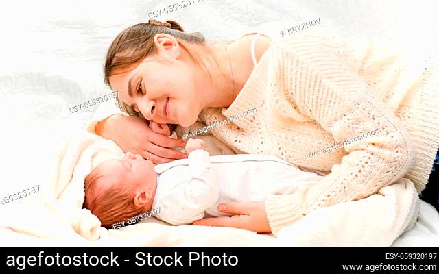 Top view of beautiful smiling mother lying next to her newborn baby and looking on son. Concept of family happiness and loving parents with little children