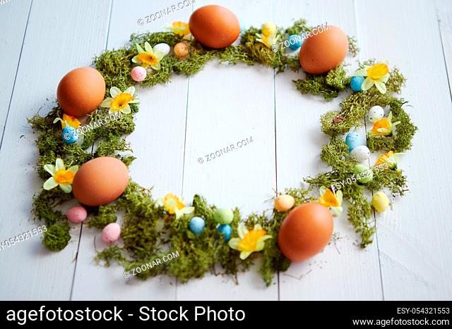 Colorful decorative Easter eggs wreath on white wooden table background. Top angle shot. Flat lay