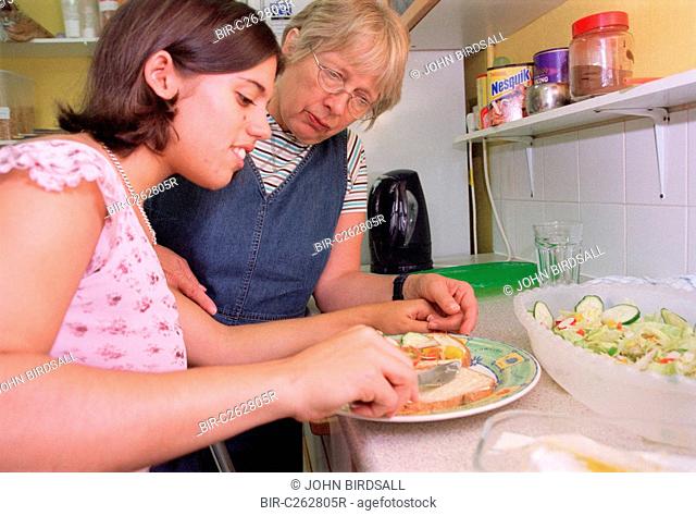 Carer assisting teenage girl with physical disability to prepare a sandwich in kitchen of residential respite care home