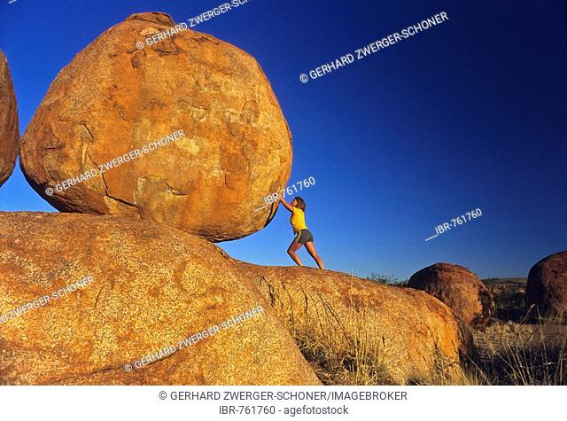 Woman propping up large round rock, Devil's Marbles, Northern Territory, Australia