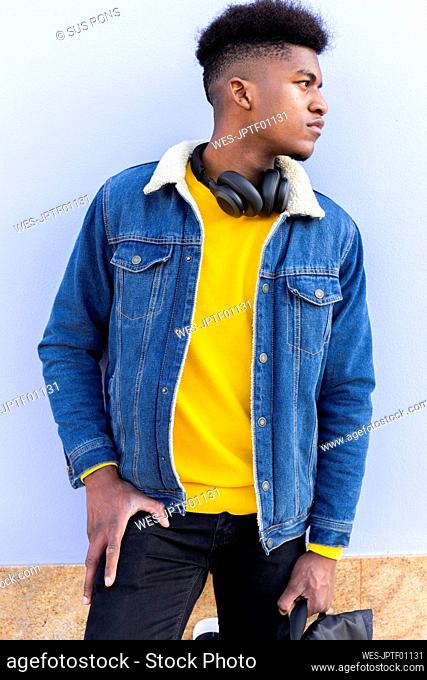 Young man wearing denim jacket standing in front of wall
