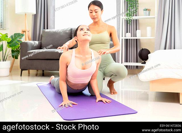 Young woman beginning yoga practice with private teacher at home. Professional instructor teaches student to do Bhujangasana exercise or Cobra pose