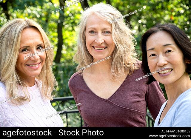 Portrait of three middle aged lady friends looking at camera while having a good time together outdoors