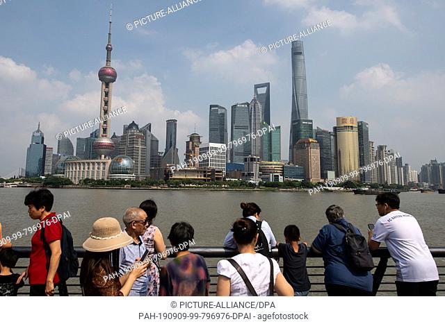 08 September 2019, China, Shanghai: Tourists stand at the promenade ""The Bund"" at the Huangpu river with a view of the skyline of the special economic zone...
