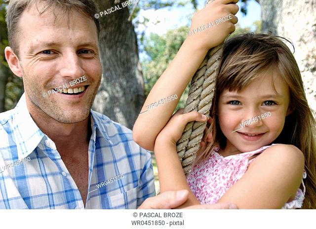 Portrait of a girl swinging on a rope swing with her father smiling beside her