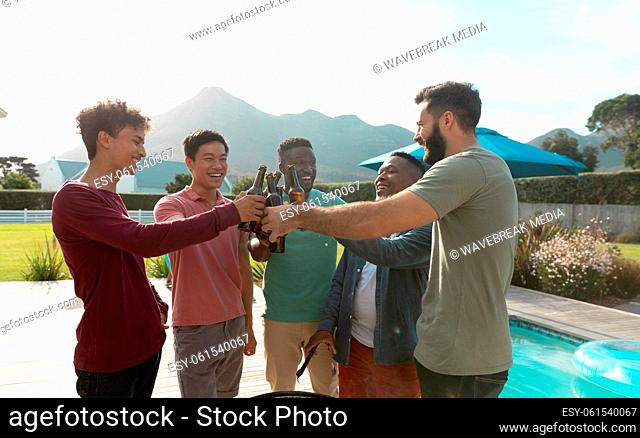 Multiracial male friends toasting beer bottles while having fun at barbecue party in backyard
