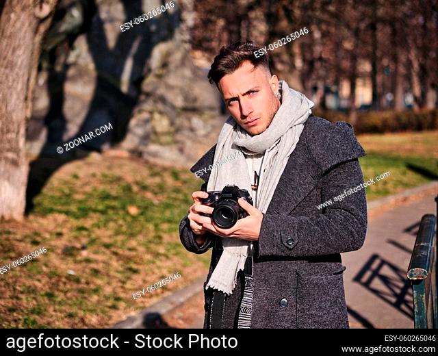 Handsome young male photographer taking photograph with professional photo camera, outdoor in city park