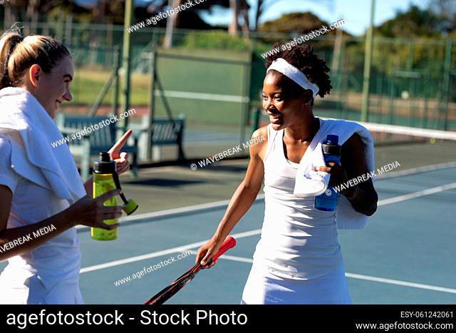 Happy biracial female tennis players talking while enjoying break at court on sunny day
