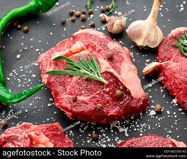 raw piece of beef ribeye with rosemary, thyme on a black table, top view