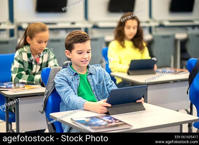 Lesson. Boy and girls sitting at desks carefully looking at their tablets studying at school
