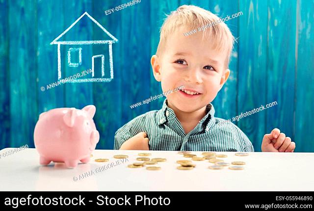 three years old child sitting st the table with money and a piggybank. Happy boy with euro coins. Kid dreaming about home