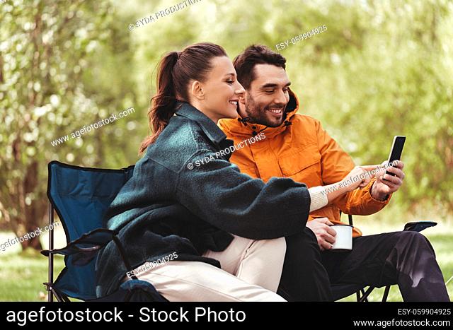 couple with smartphone drinking tea at campsite