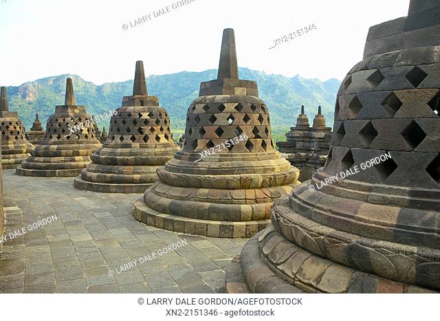 View of the Menoreh Hills and Kedu Plain through some of the 72 stupas atop the 9th-Century Mahyana Buddhist Temple at Borobudur, Central Java, Indonesia