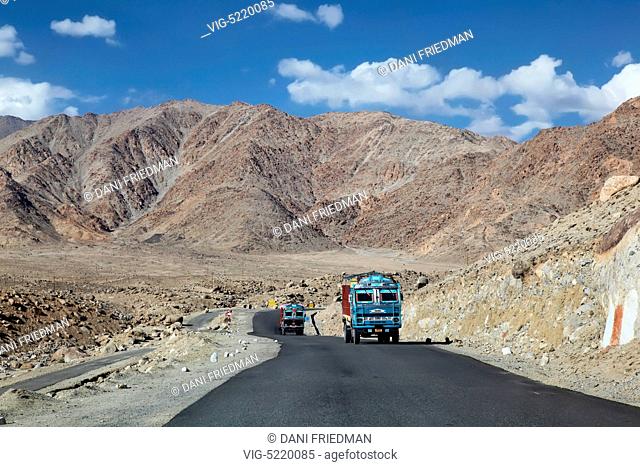 Two trucks carrying goods travel along an isolated road cutting through the Himalayas in Ladakh, Jammu and Kashmir, India