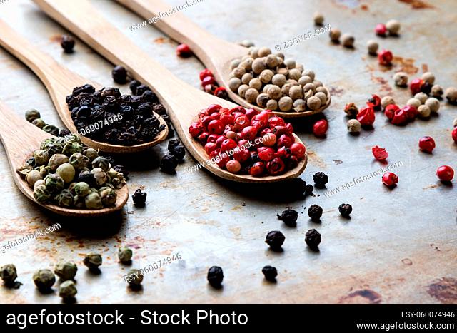 different color peppercorn seeds on wooden spoons on steel plate