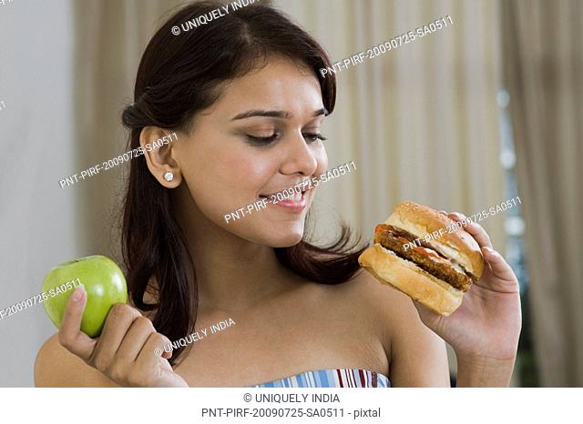 Woman holding a burger and a green apple