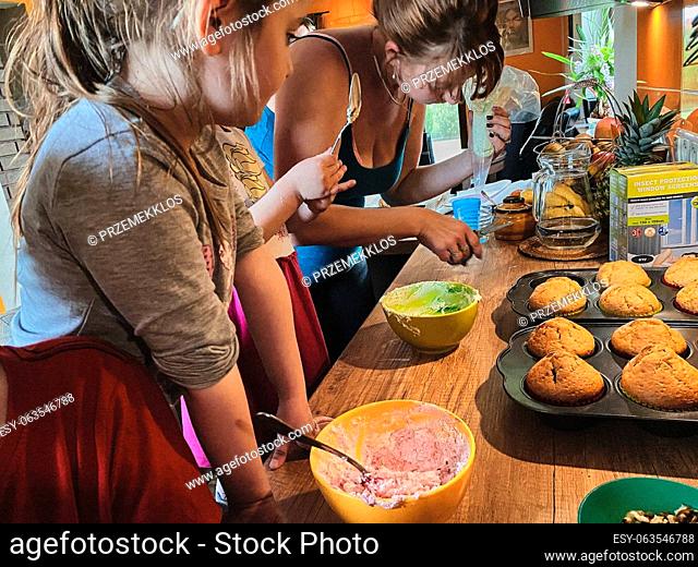 Group of children baking cupcakes, preparing ingredients, toppings, sprinkles for decorating cookies. Kids learning to cook, working together in kitchen at home