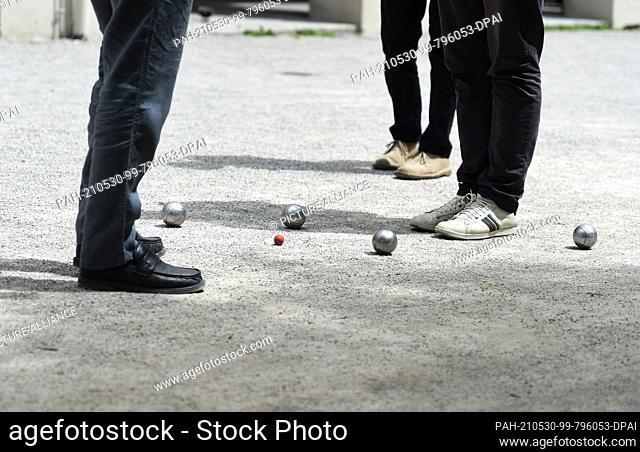 30 May 2021, Bavaria, Munich: Under a white-blue sky, boules players stand next to boules balls in the courtyard garden. Sunshine and pleasantly warm...