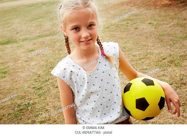 High angle view of girl with pigtails holding soccer ball looking at camera smiling