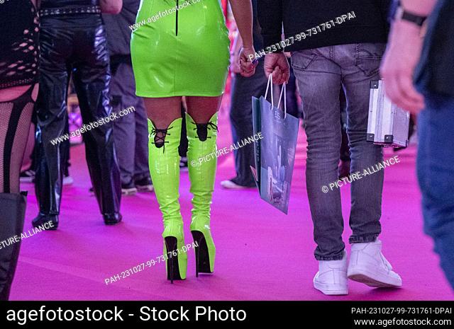 27 October 2023, Berlin: A woman with patent boots and patent outfit in neon colors walks through a hall at the erotic fair Venus 2023