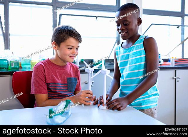 Caucasian boy and african american boy holding windmill models in science class at elementary school